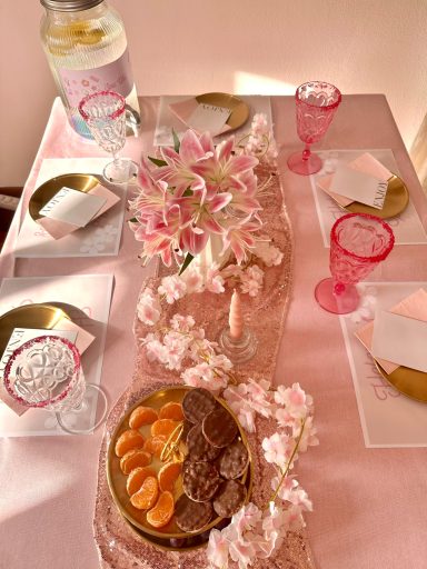 Tischgedeck mit rosa Lilien, Tellern, Gläsern und einer Obstschale. Spa Party