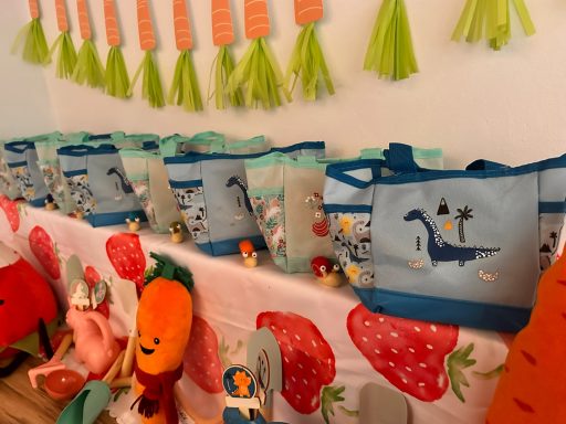 Gartenwerkzeugtaschen Farbenfrohe Tasche mit Dinosaurier-Motiv auf einem Tisch mit Spielzeug und Dekoration für den Gartenzwerge Kindergeburtstag.