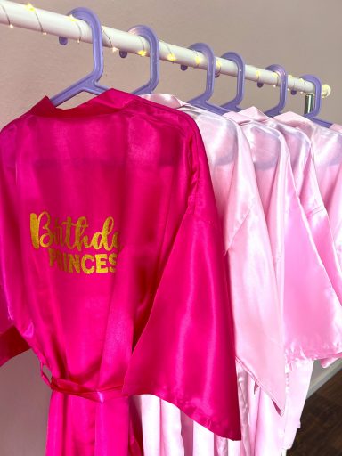 Rosa und pinke Morgenmäntel hängen an einer Stange. Ein Mantel hat den Schriftzug Birthday Princess.